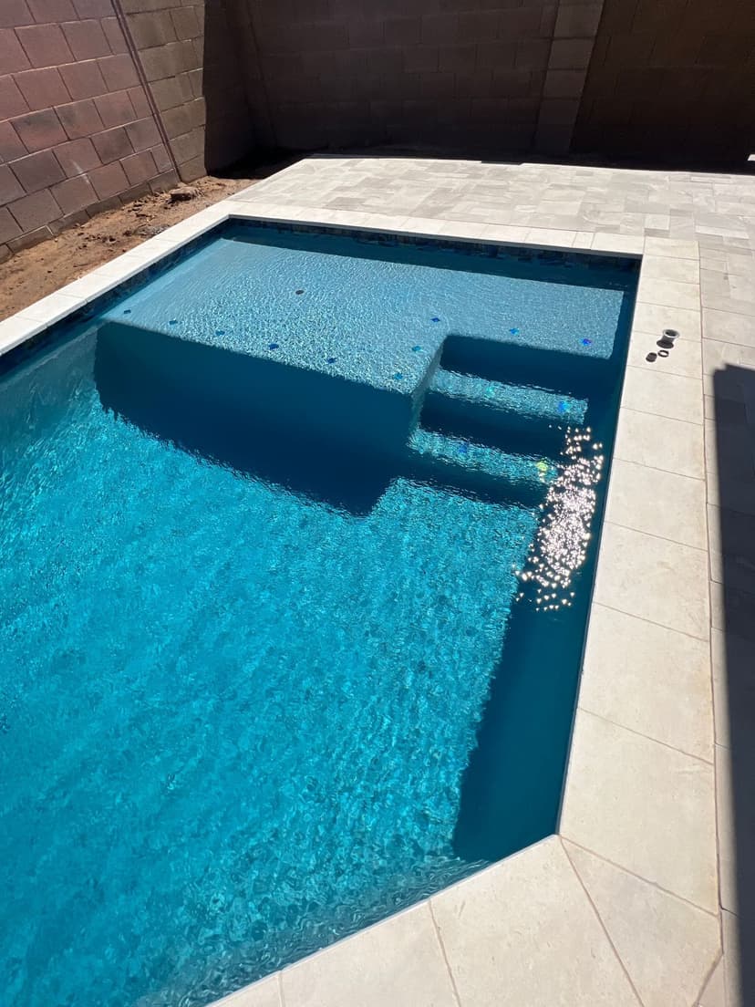 Geometric pool with a large baja shelf, steps, and light paver deck